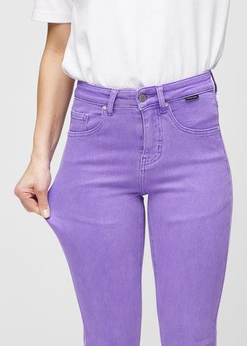 Slim jeans for women in purple, color Lavenders. A model stretches the jeans at the thigh to show the fabric&