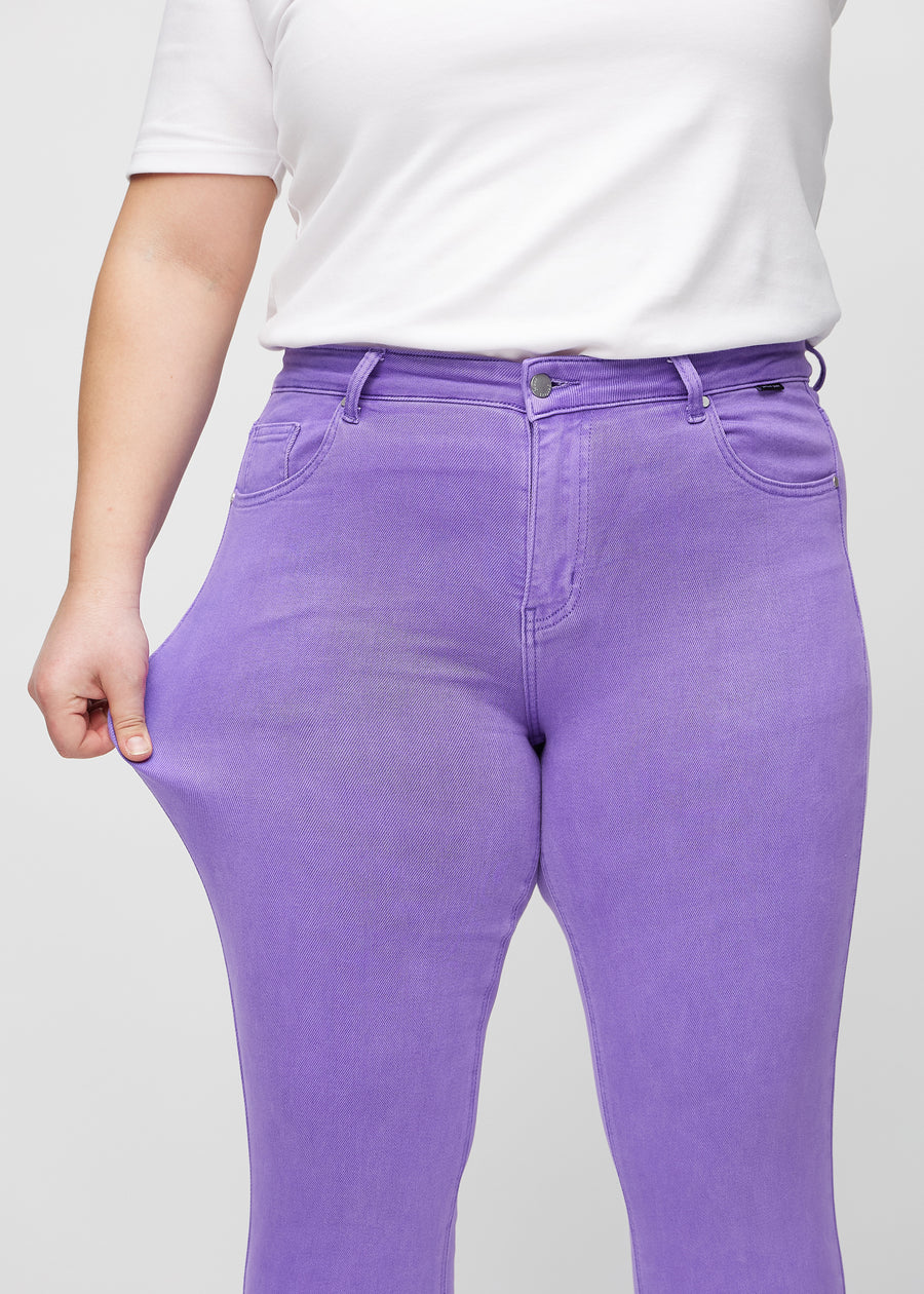 Slim jeans for women in purple, color Lavenders. A plus-size model stretches the jeans at the thigh to show the fabric&