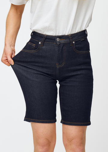 Model stretches deep dark blue denim shorts for women in the colour Midnights at the thigh to show the material’s stretch.