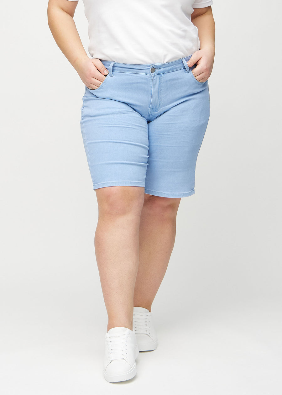 Light blue regular middle shorts, model name Skies, which fall straight down the leg and end just above the knee on a plus-size model, seen from the front.