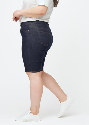 Deep dark blue denim shorts for women in the colour Midnights with a skinny fit seen from the side on a plus-size model.