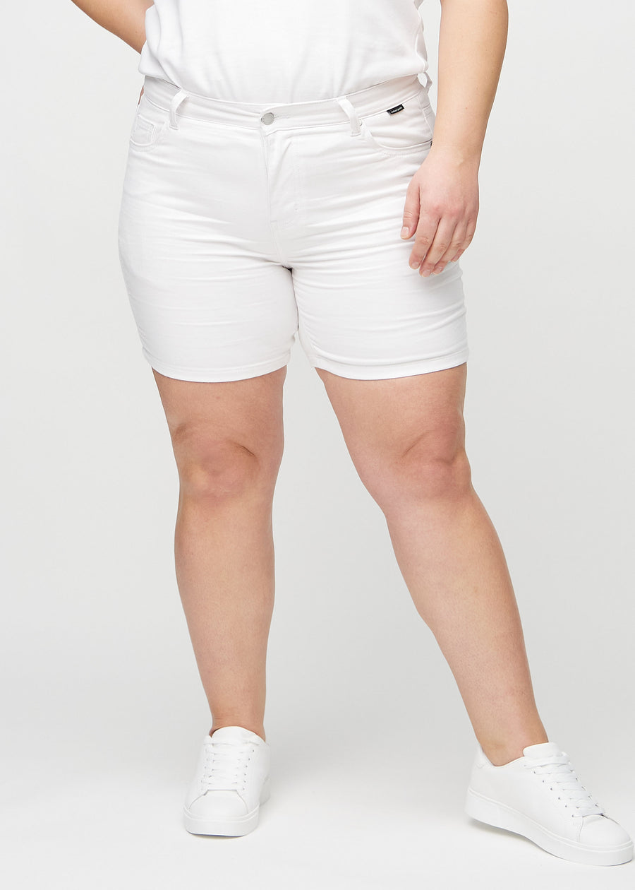 White skinny short shorts, style name Marguerites, which fit closely and end mid-thigh on a plus-size model, seen from the front.