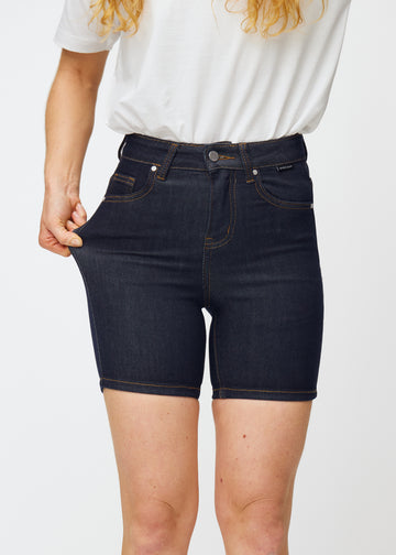 Model stretches deep dark blue denim shorts for women in the colour Midnights at the thigh to show the material’s stretch.