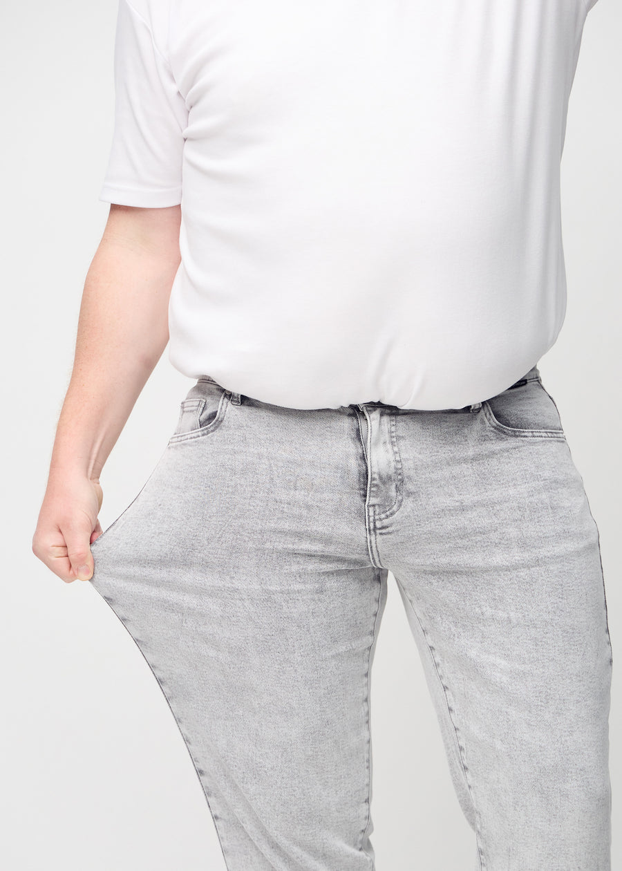 The plus-size model stretches the jeans at the thigh to show the stretch.