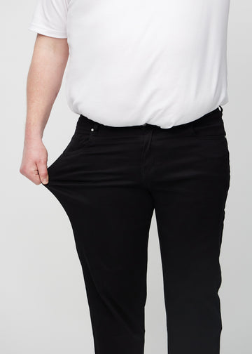 The plus-size model stretches the jeans at the thigh to show the stretch.