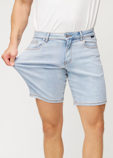 The model stretches the light blue denim shorts for men in the colour Waves at the thigh to show the material&