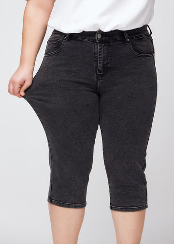 Plus-size model viser stretch ved at trække i caprisene ved låret – fokus på komfort og fleksibilitet i den mørkegrå denim.