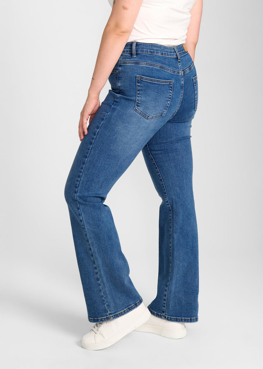 Mørkeblå denim bootcut jeans, modelnavn Oceans, som sidder tæt om hofter og lår med et let svaj fra knæet og ned, set fra siden på model på en plus-size model.
