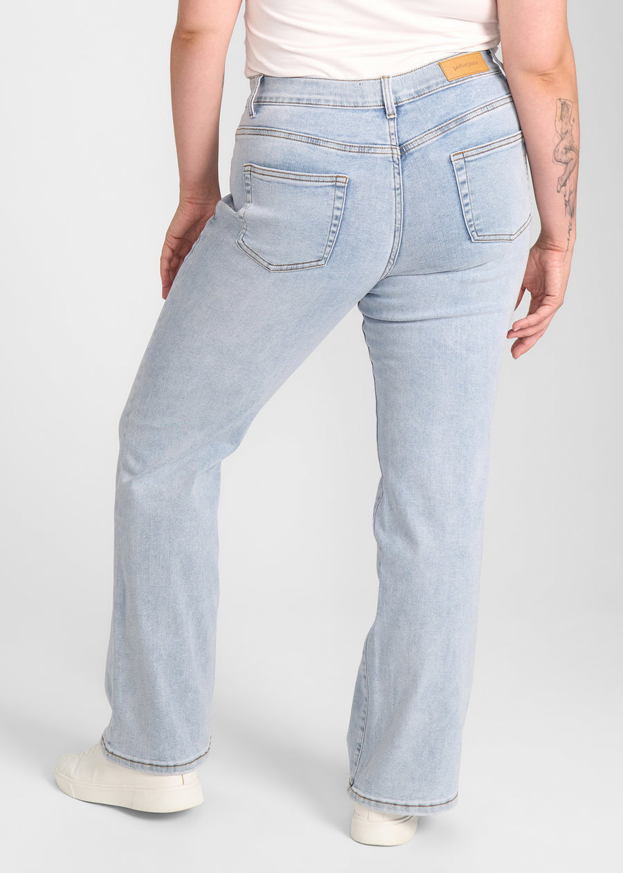Lyseblå denim bootcut jeans, modelnavn Waves, som sidder tæt om hofter og lår med et let svaj fra knæet og ned, set bagfra, så man kan se hele produktet. på en plus-size model.