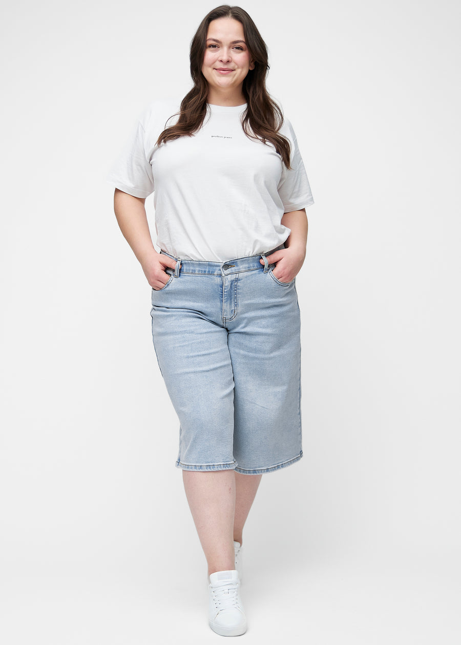 Plus-size model viser løse, lyseblå denim capris i farven Waves i bevægelse og demonstrerer pasform og materiale.