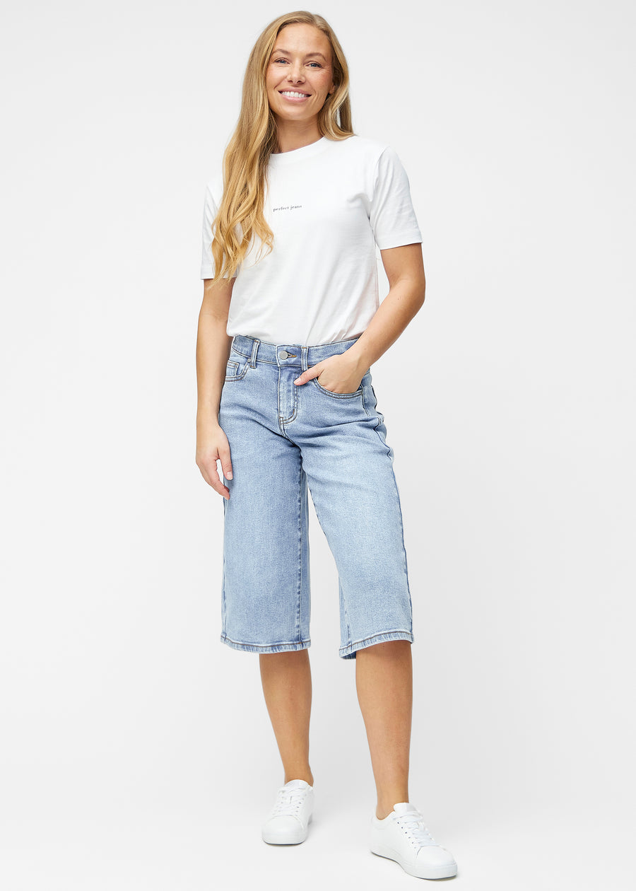 Model viser løse, lyseblå denim capris i farven Waves i bevægelse og demonstrerer pasform og materiale.