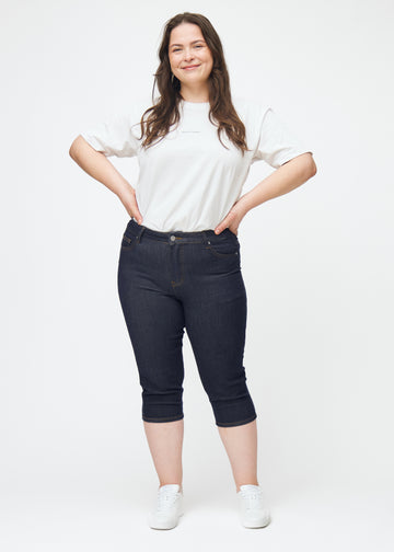 Plus-size model viser dyb mørkeblå denim capris til kvinder i farven Midnights med skinny pasform i bevægelse.