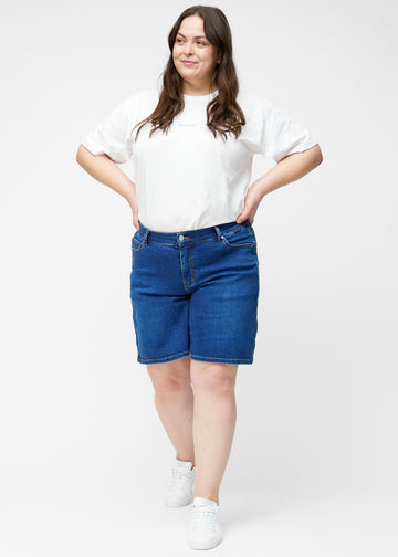Plus-size model viser løse, mørkeblå denim shorts i farven Oceans i bevægelse og demonstrerer pasform og materiale.