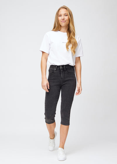 Model træder ind i billedet, strækker i sine mørkegrå denim slim capris, viser dem frem ved at dreje rundt, og går derefter ud af billedet igen.